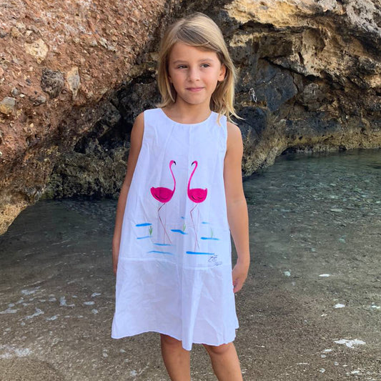 Este vestido blanco de estilo ibicenco para niñas destaca por la calidad de su tejido y por la estética única de los flamencos pintados a mano